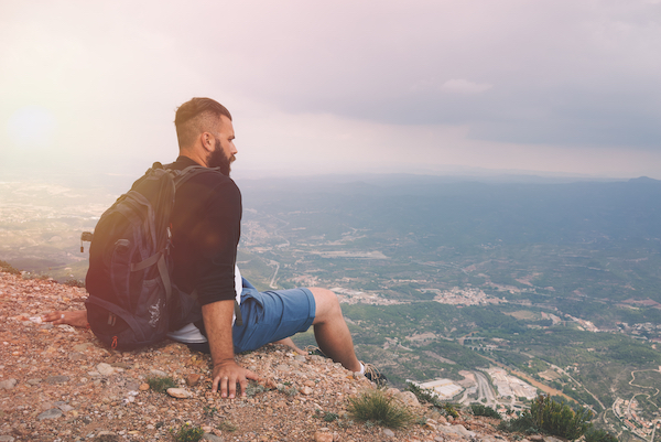 Man in Shorts Sitting on Mountain, looking at view